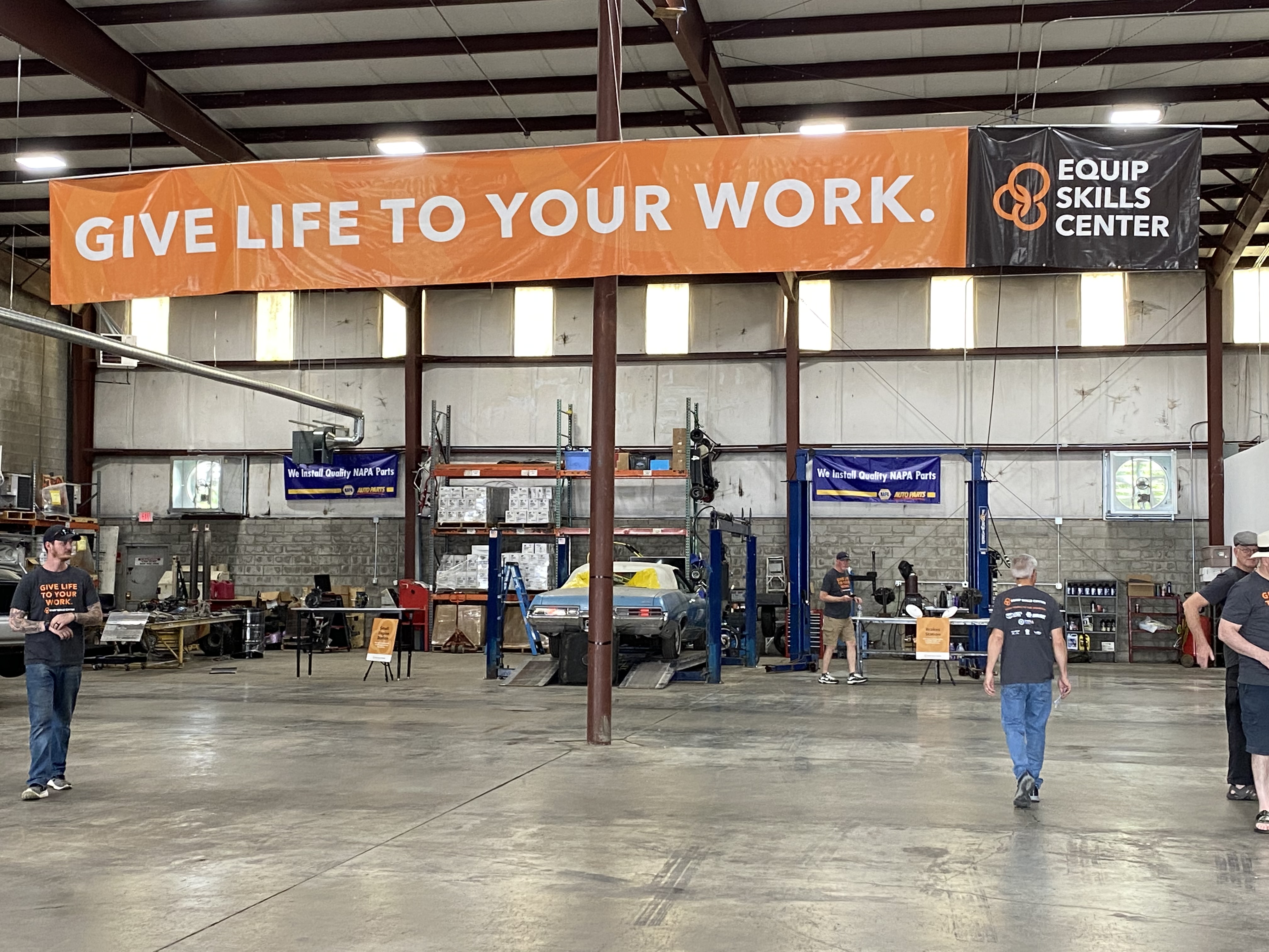 A photo of the Equip Skills Center garage. A few people are at work in the garage under a banner that reads "Give life to your work."